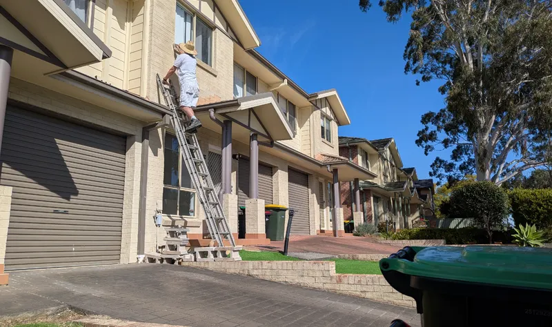 Painter spraying and back-rolling a red brick home exterior